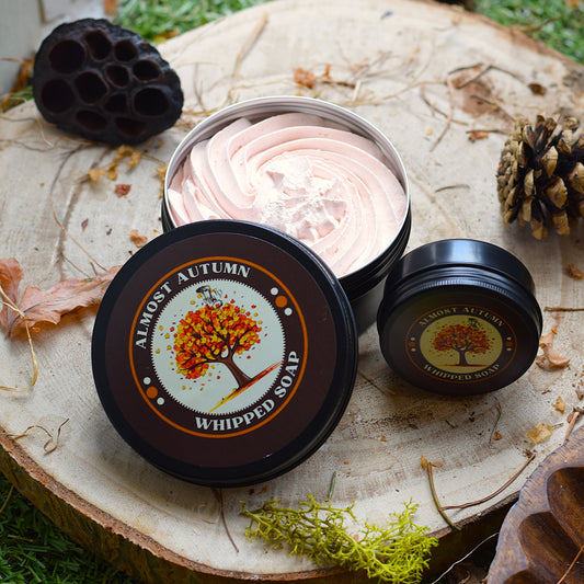 Whipped soap in a container with 'Almost Autumn' branding on a natural background.