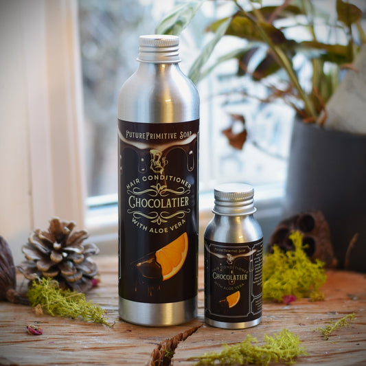 Two metal bottles labeled 'Chocolatier' on a wooden surface with plants in the background.