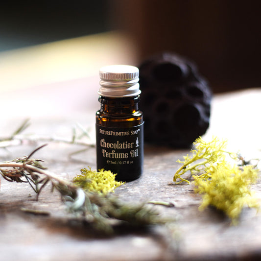 Perfume oil bottle labeled 'Chocolatier' on a wooden surface with greenery