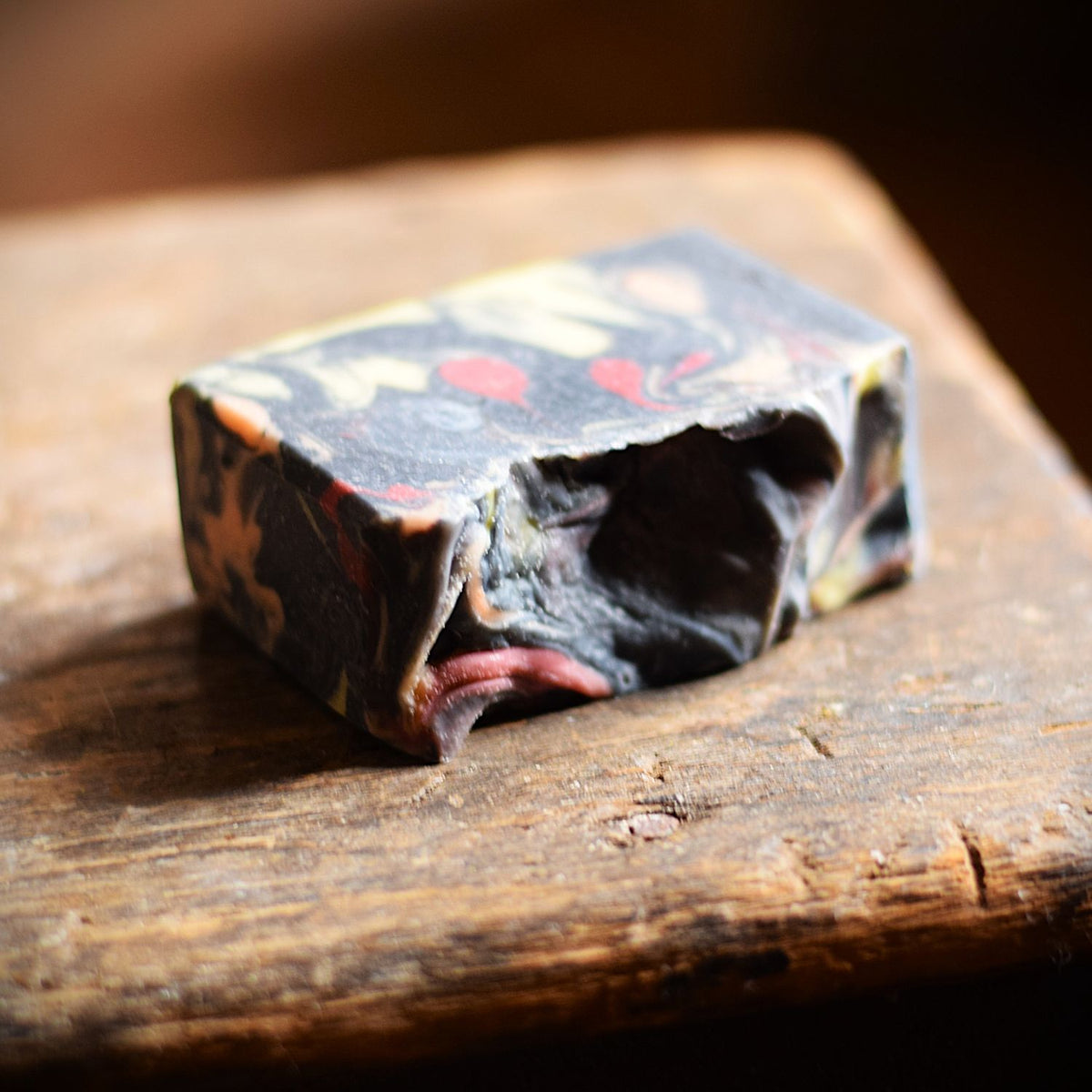 a bar of marbled soap sits on a rustic wooden table. the soap is in focus at the front and the background is blurred.