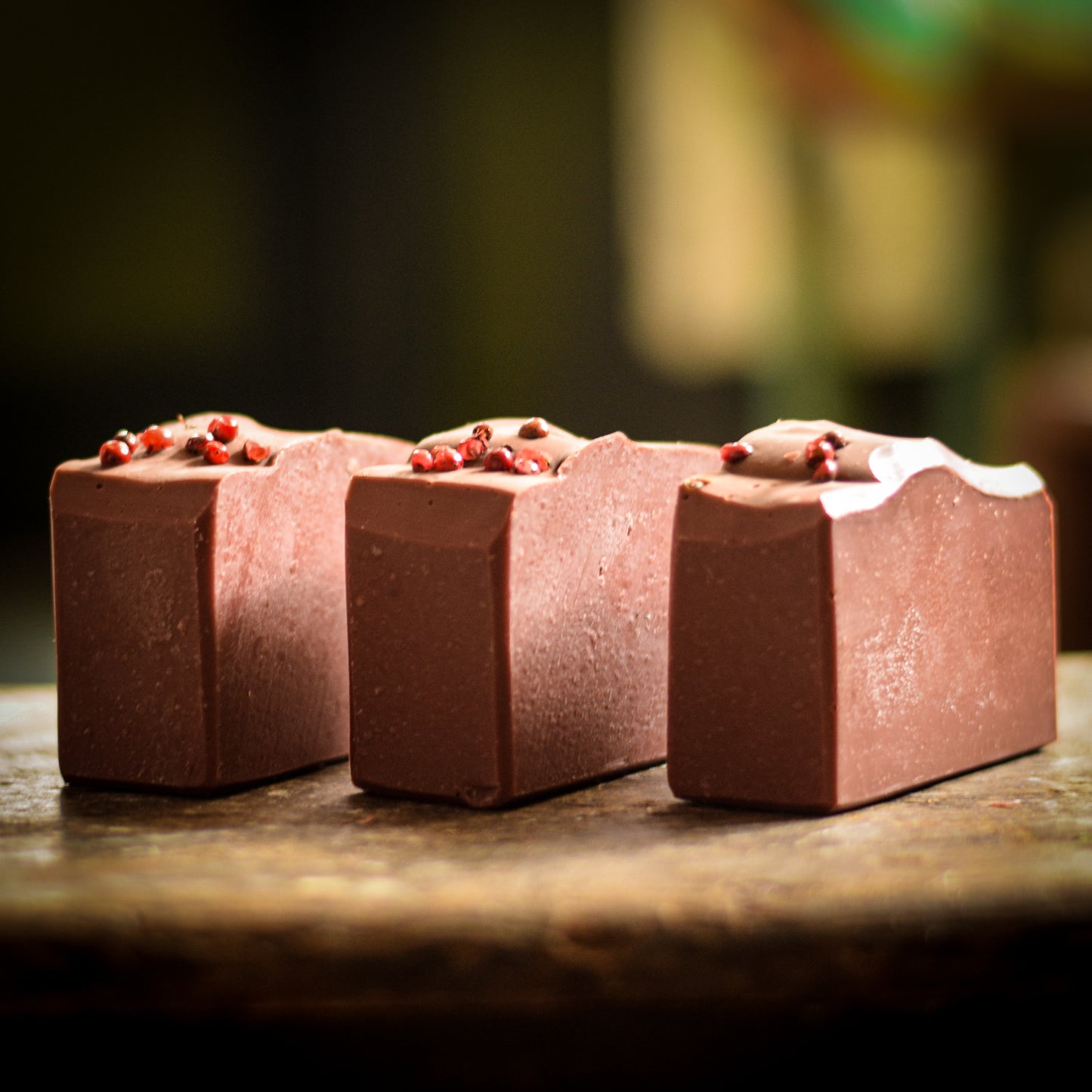 Three clay soap bars with red peppercorns on a wooden surface