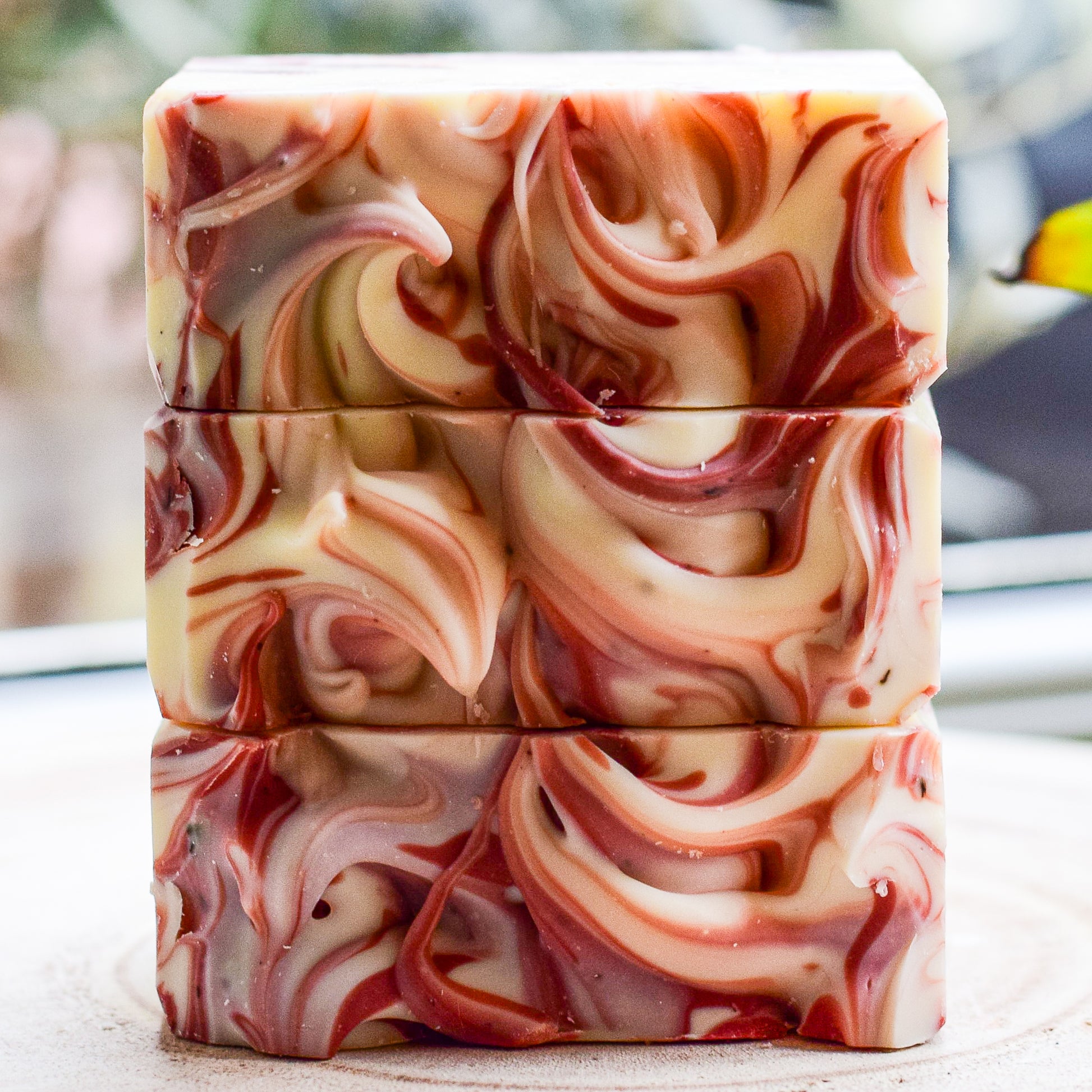 Stack of red clay marbled soap bars on a light surface with blurred background