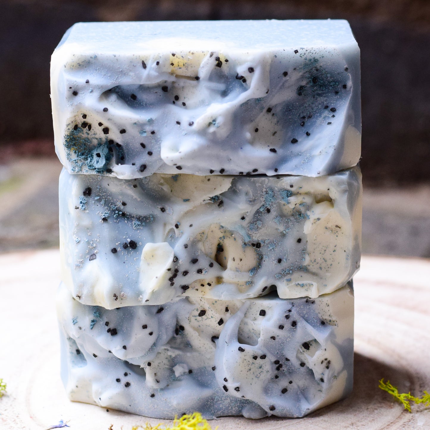Stack of three blue and white natural handmade soap bars with visible specks on a wooden surface