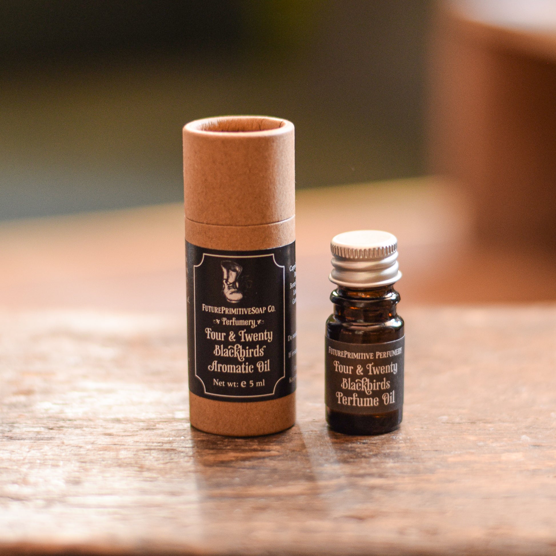 Two perfume bottles, one in a cardboard tube and the other in a small glass bottle, on a wooden surface.