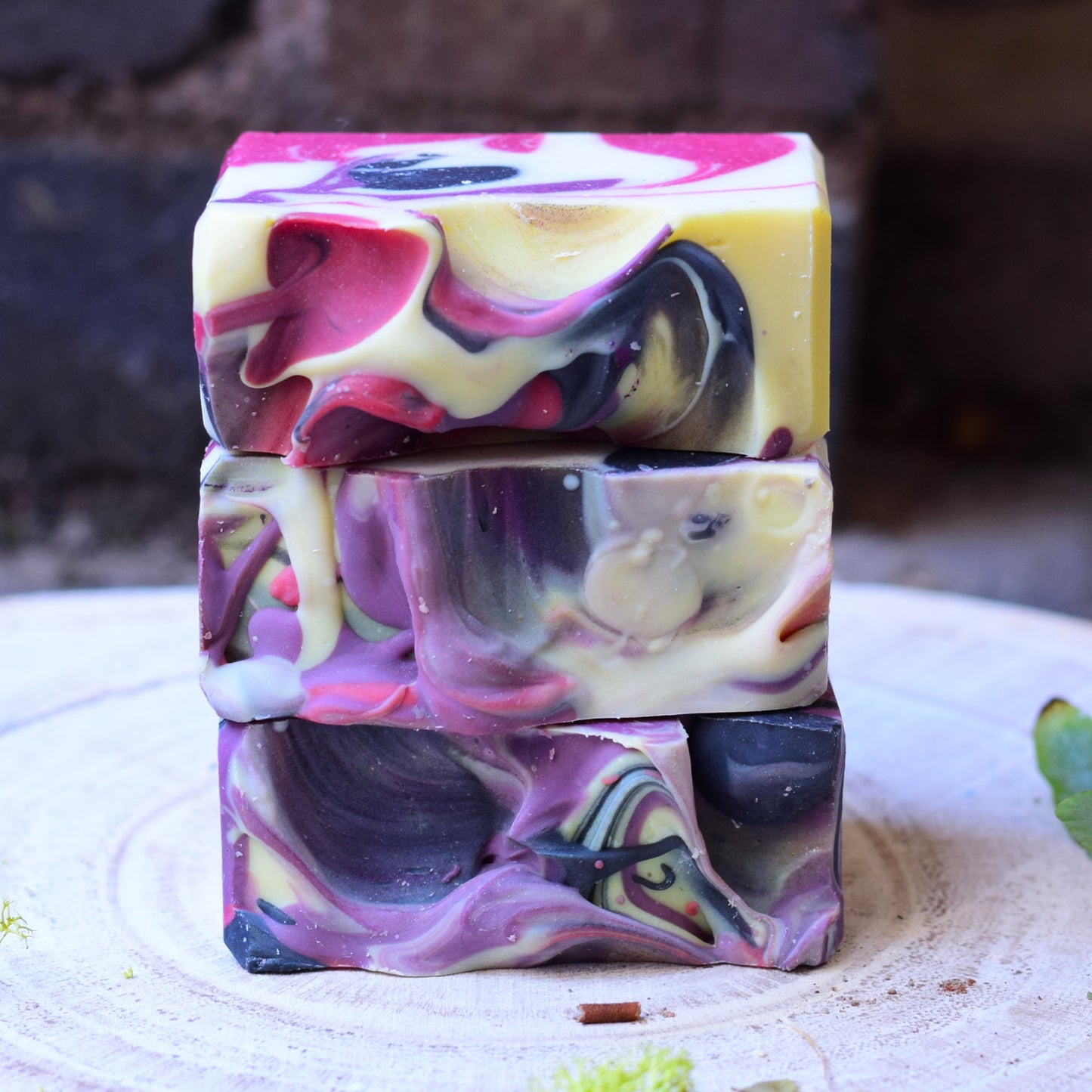 Stack of multicolored soap bars on a textured surface with a blurred natural background