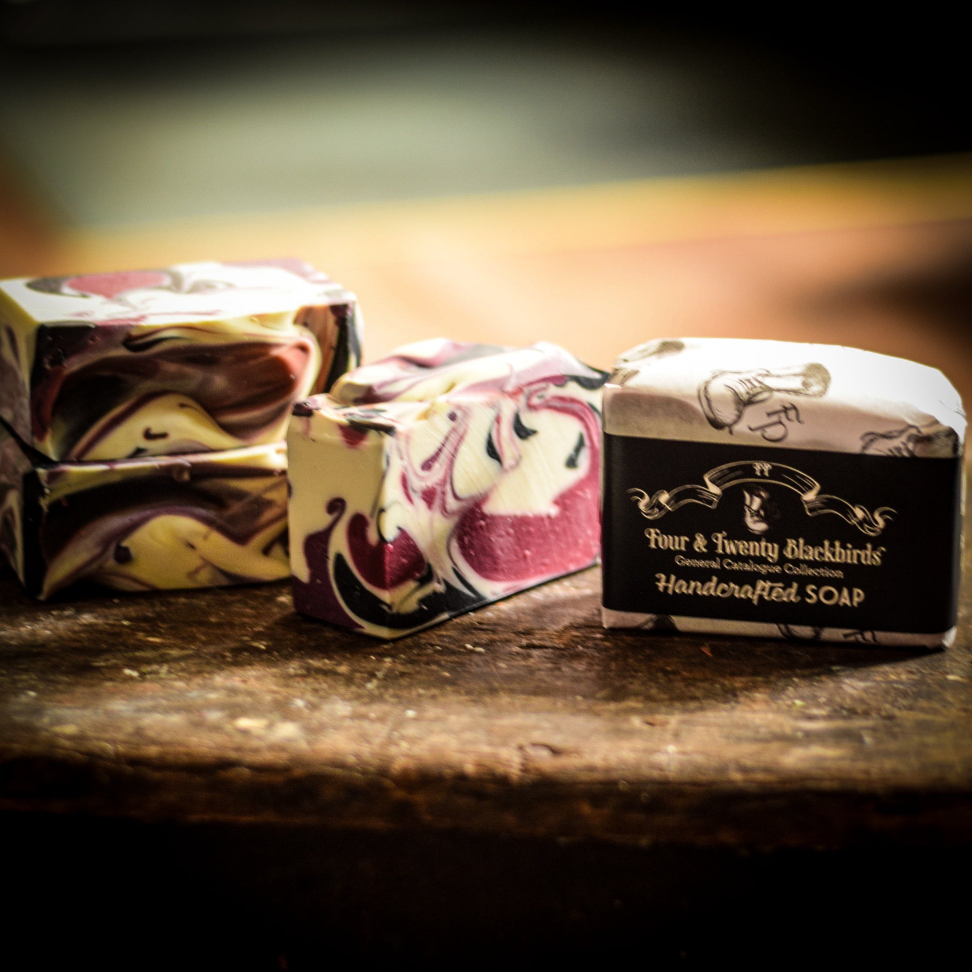 Three bars of handmade artisan soap with marbled designs on a wooden surface, featuring the name 'Four & Twenty Blackbirds'.