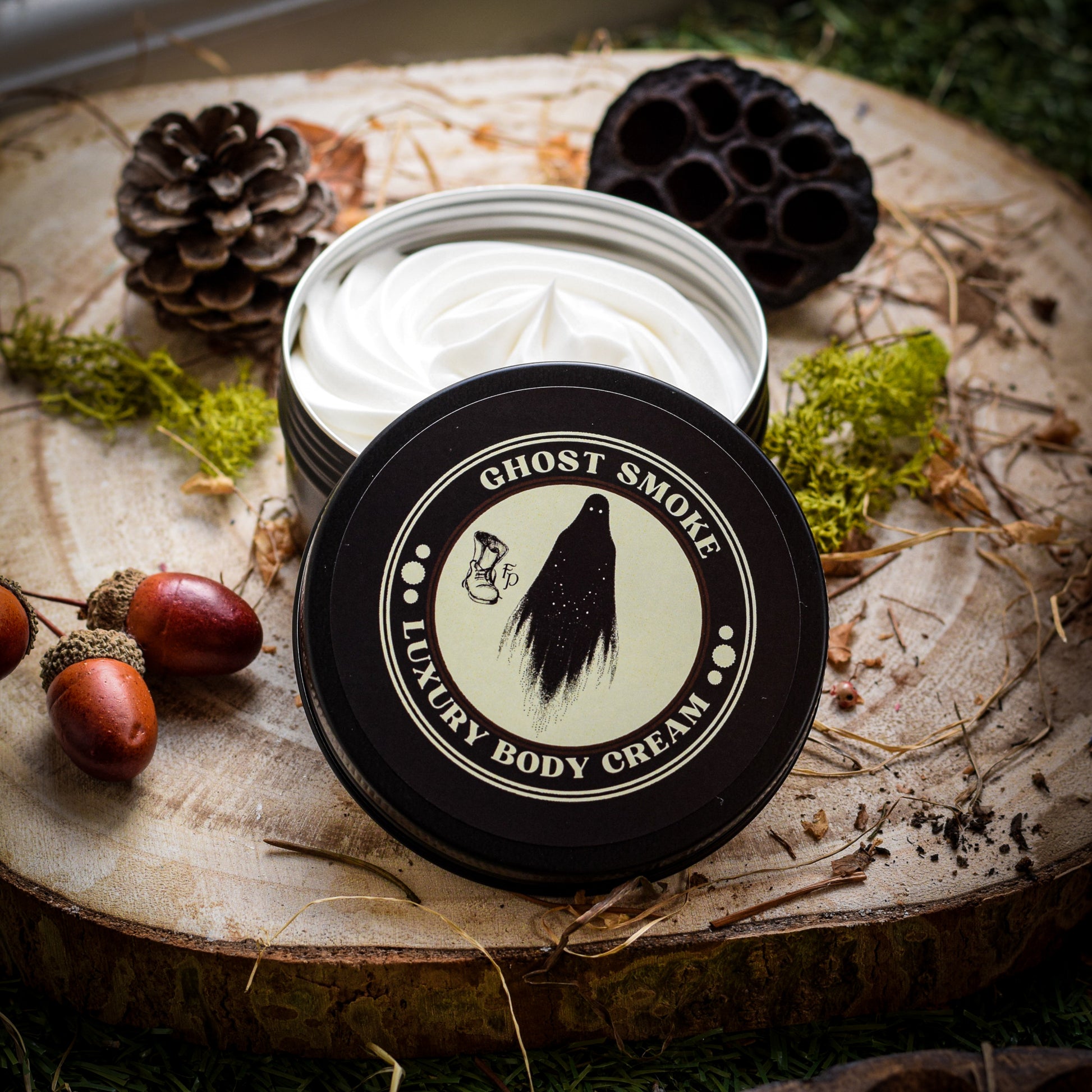 Ghost Smoke Luxury Body Cream sat on a wooden plinth surrounded by seed pods and moss