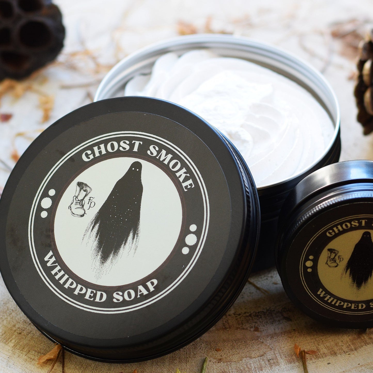 Ghost Smoke whipped soap in a black container on a wooden surface with natural elements.