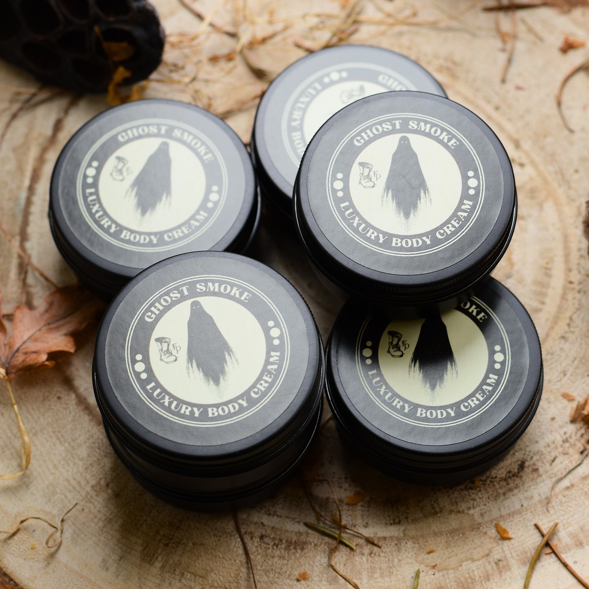Five containers of Ghost Smoke Luxury Body Cream on a rustic wooden surface.