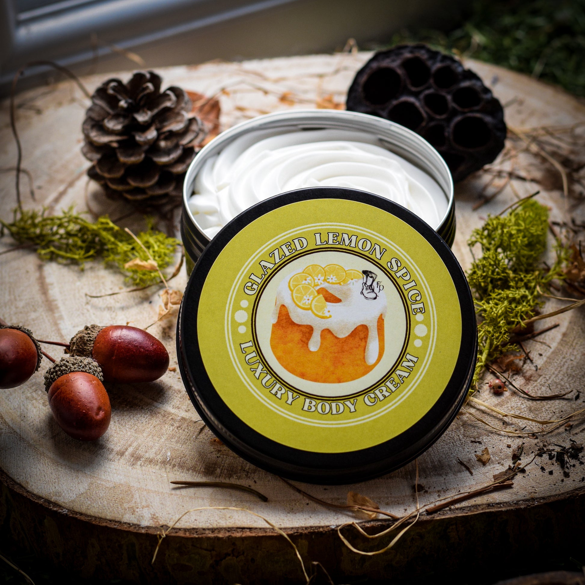 Glazed Lemon Spice luxury body cream sitting on a wooden plinth surrounded by dried seeds and moss