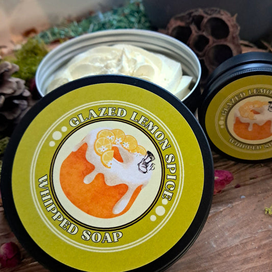 Two containers of 'Glazed Lemon Spice' whipped soap on a wooden surface with decorative elements.