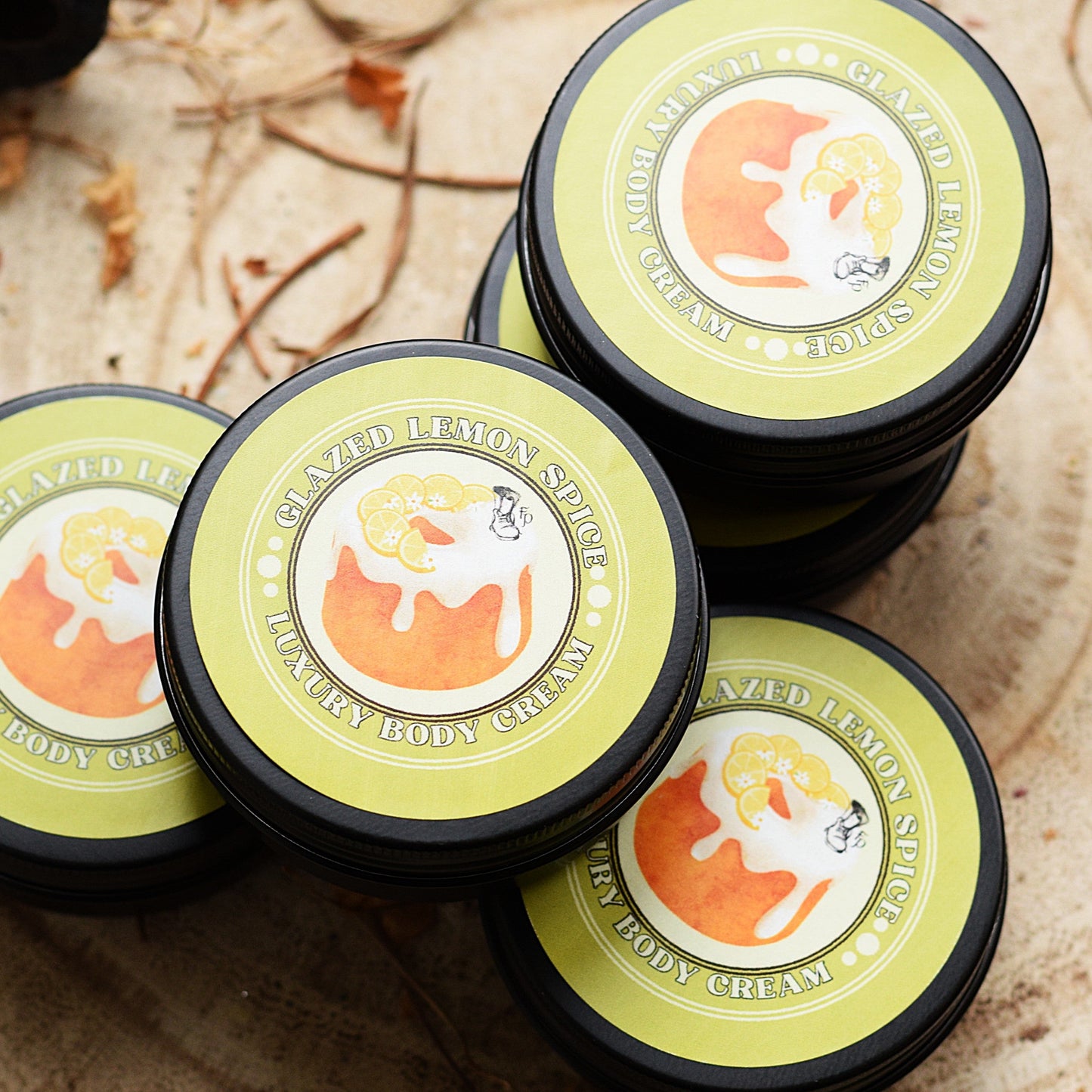Four containers of lemon spice body cream on a wooden surface with leaves.
