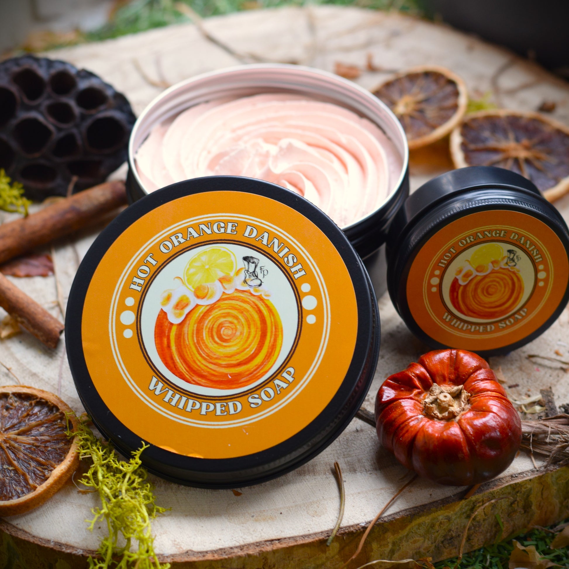 Two containers of 'Hot Orange Danish' whipped soap on a rustic wooden surface with autumn elements.