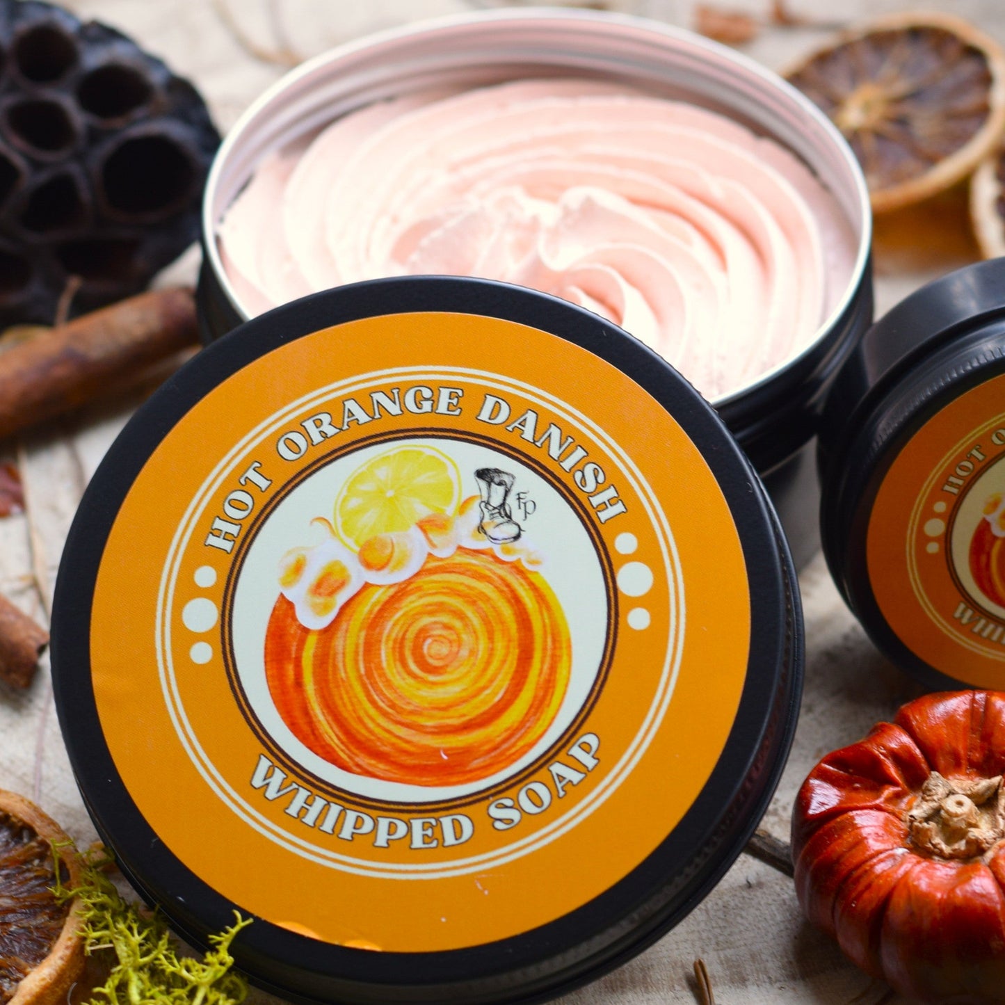 Two containers of 'Hot Orange Danish' whipped soap on a rustic wooden surface with autumn elements.