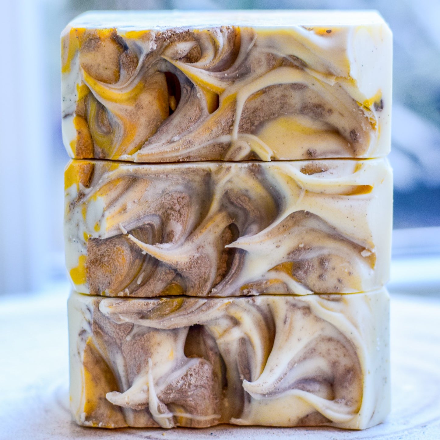 Three bars of soap with a swirled pattern in brown, yellow, and white on a light background.
