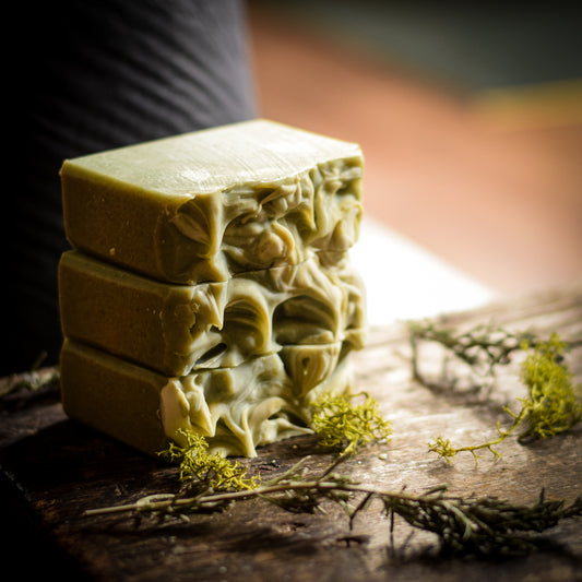 Stack of green soap bars on a wooden surface with herbs