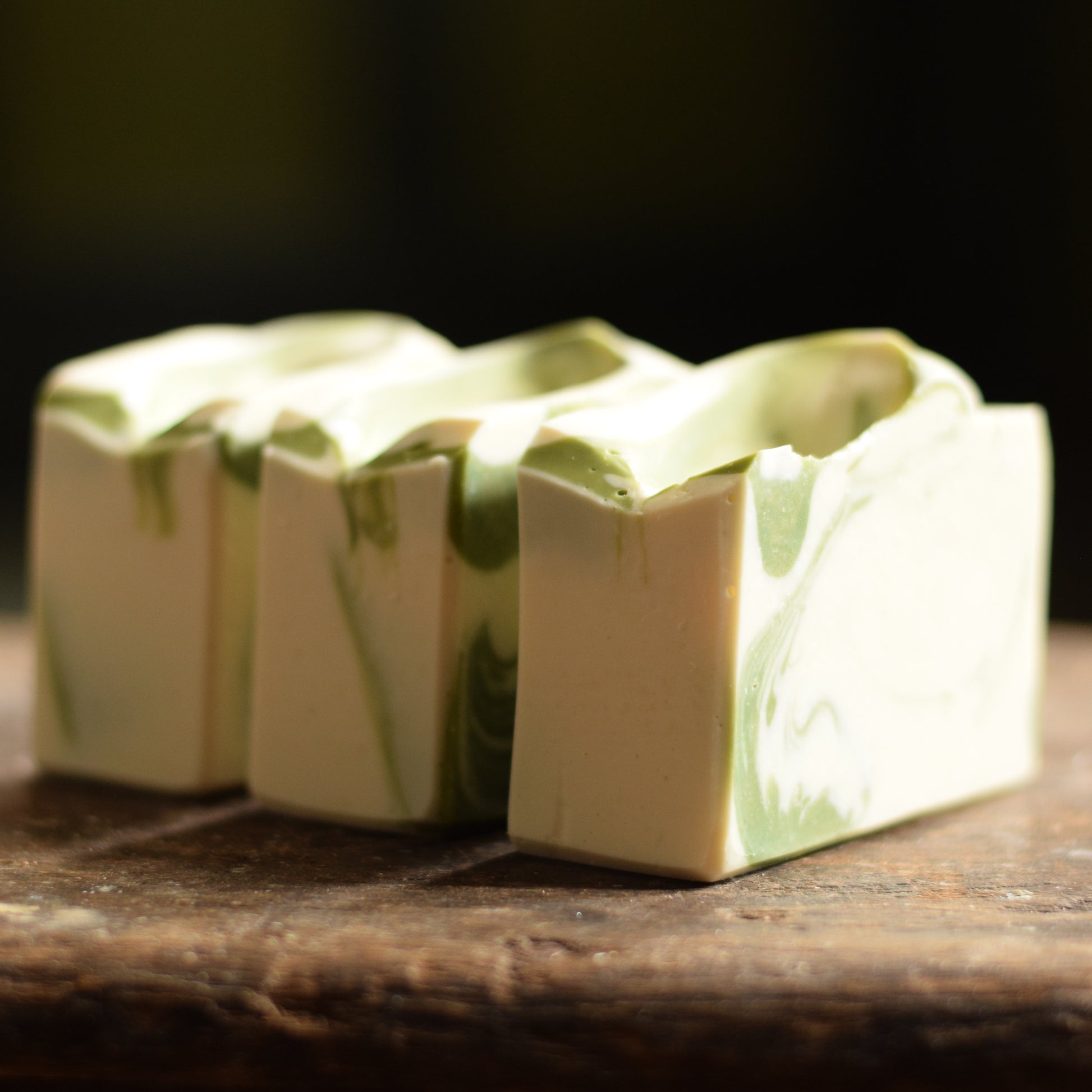 Three blocks of soap on a wooden surface with a dark background