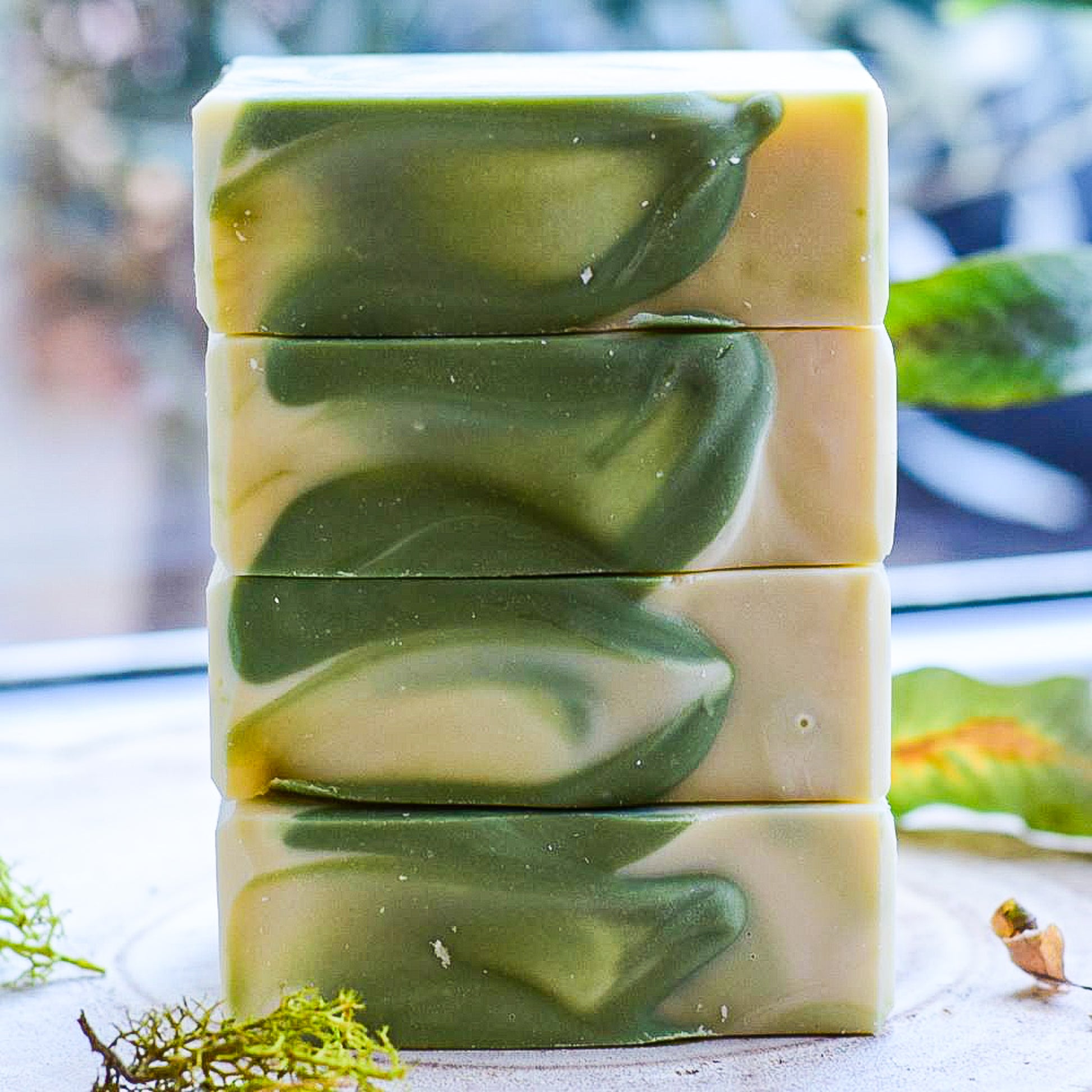 Stack of green and white swirled soap bars on a blurred natural background