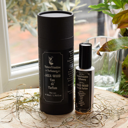 Perfume bottle and packaging on a wooden surface with a window and plant in the background