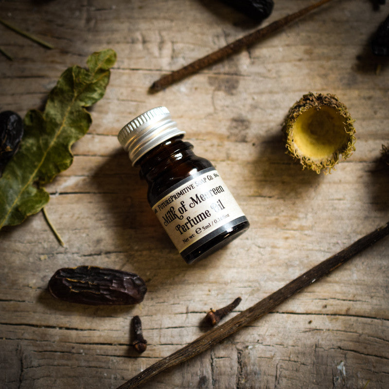 Small bottle of perfume labeled 'Milk of Meereen' on a wooden surface with natural elements.