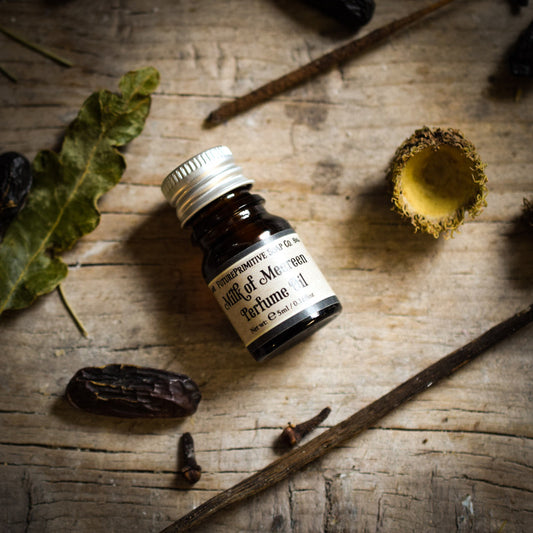 Small bottle of perfume labeled 'Milk of Meereen' on a wooden surface with natural elements.
