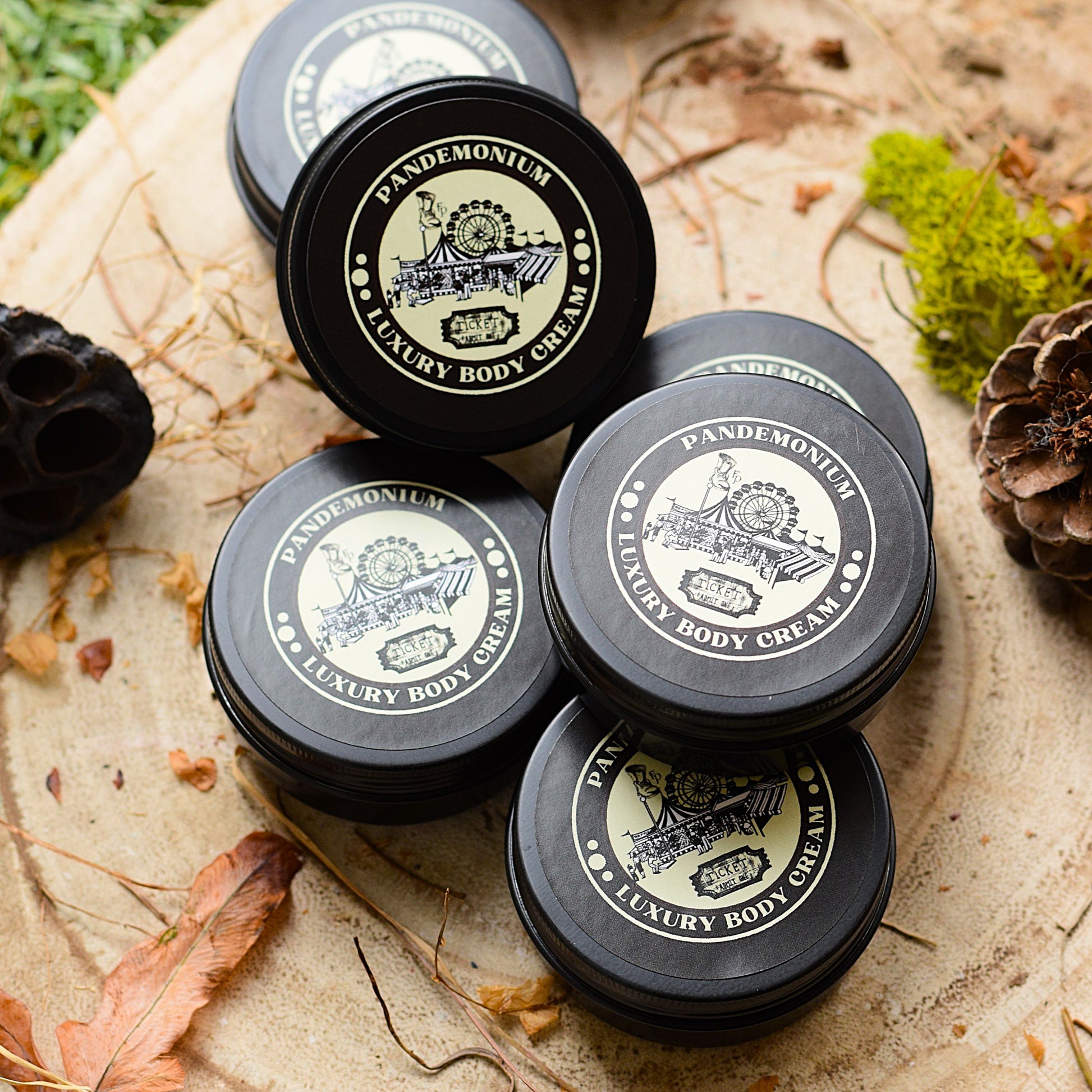 Pandemonium Luxury Body Cream jars on a natural background with leaves and pine cones.