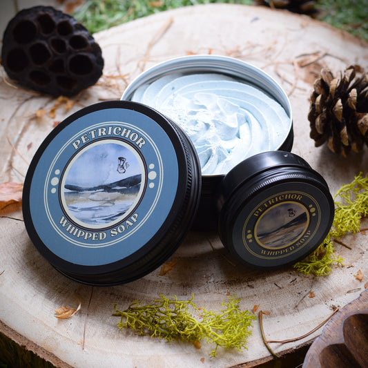 Petrichor whipped soap sat on a wooden table surrounded by moss and pine cones