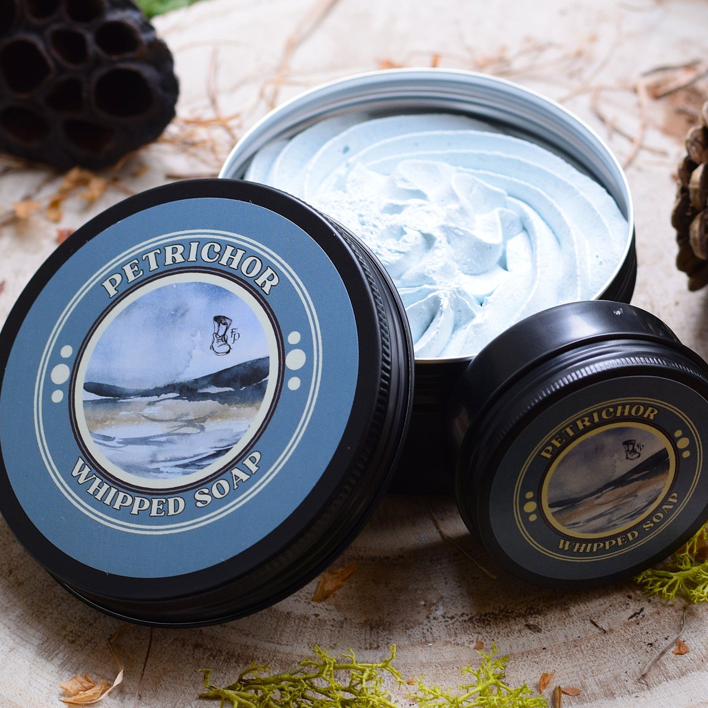 Petrichor whipped soap sat on a wooden table surrounded by moss and pine cones