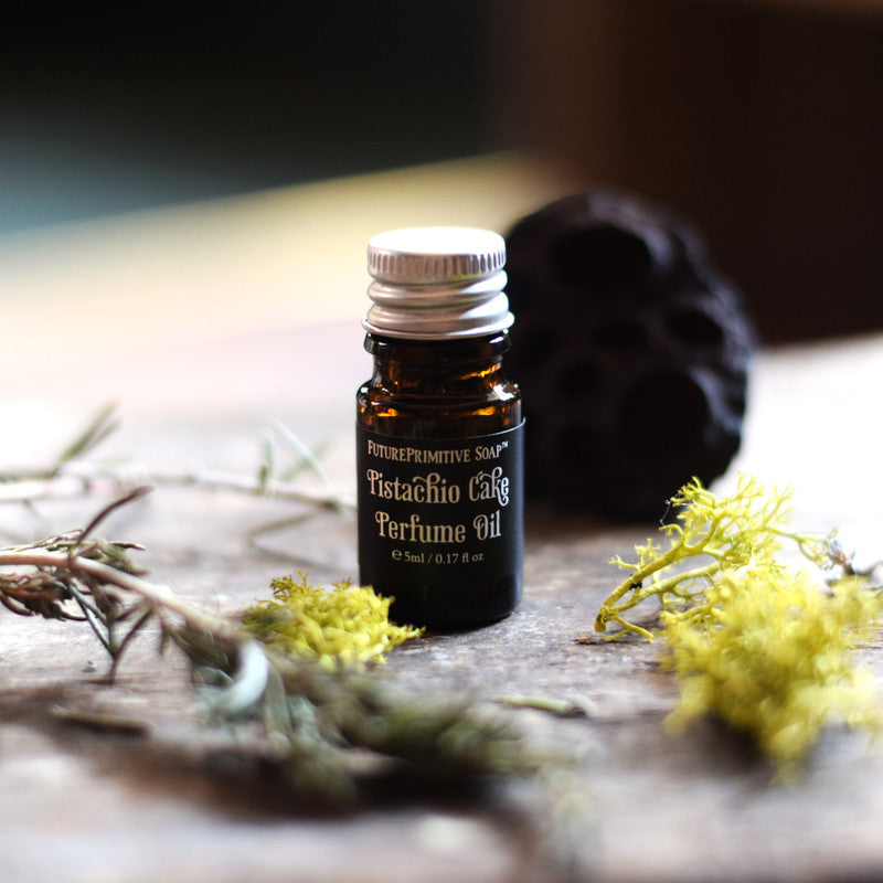 Bottle of Pistachio Cafe perfume oil on a wooden surface with greenery