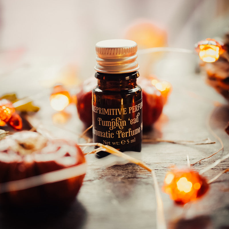 Small bottle of 'Pumpkin'ead' aromatic perfume on a wooden surface with blurred lights in the background.