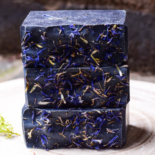 stack of charcoal soap with dried cornflowers on top with a blurred background