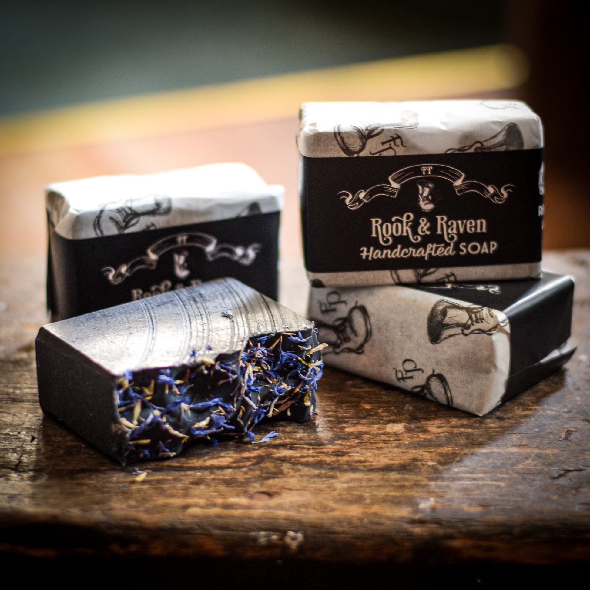 Handmade artisan soap bars with decorative wrapping on a wooden surface, featuring the name 'Rook & Raven'.