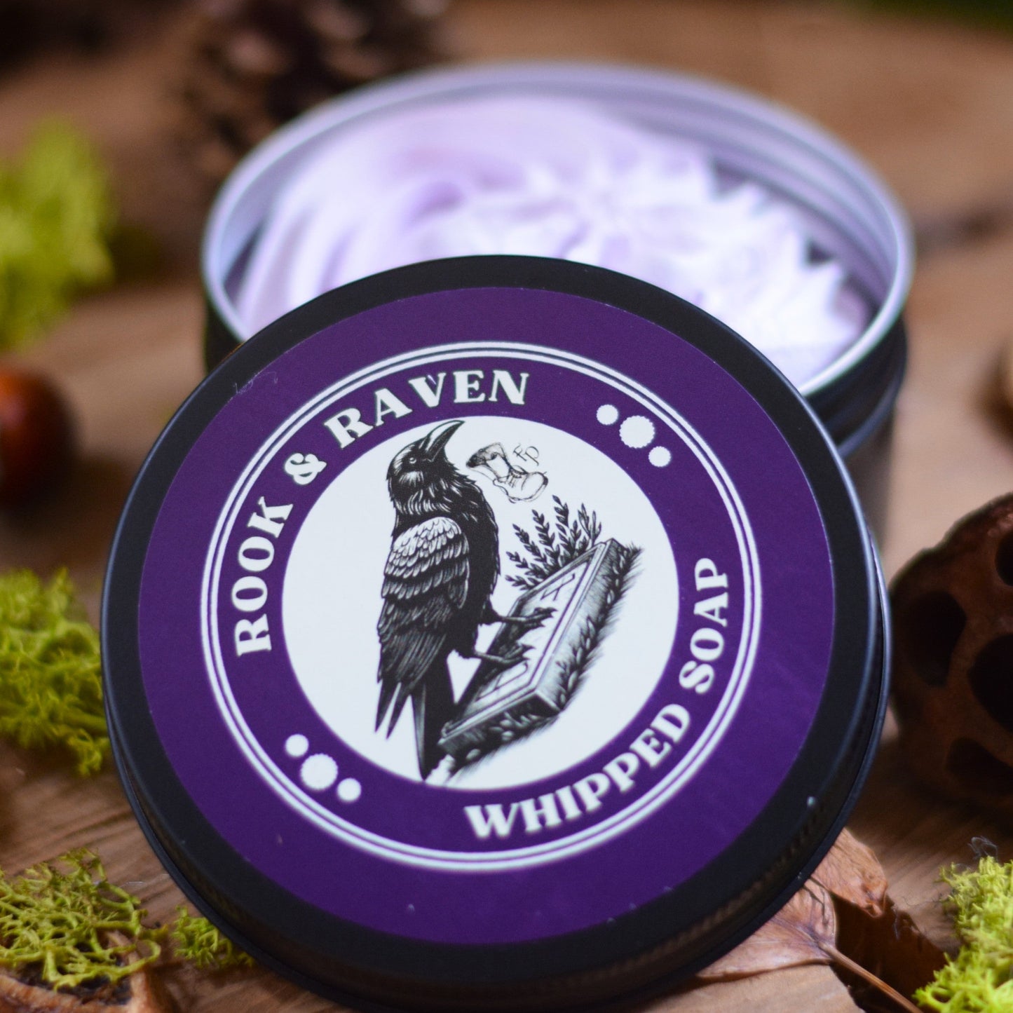 Container of Rook & Raven whipped soap on a wooden surface with natural elements.
