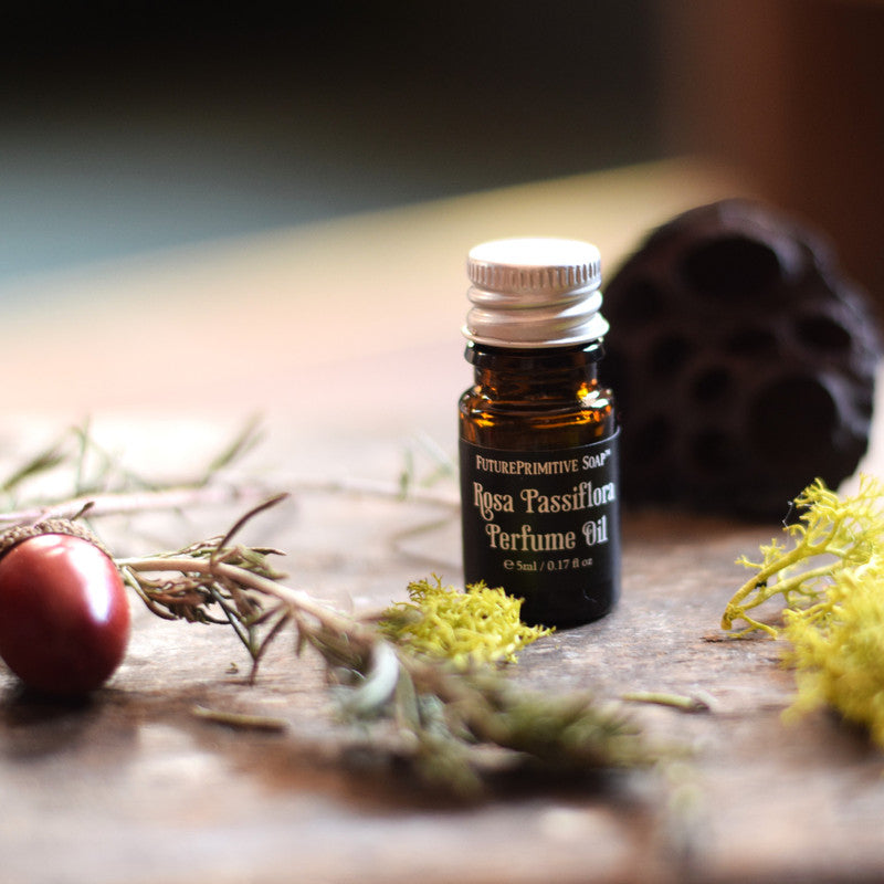 Bottle of Rosa Passiflora Perfume Oil on a wooden surface with natural elements.