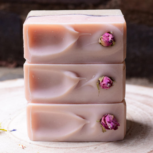 Stack of three pink handmade soap bars with dried rose buds on a wooden surface