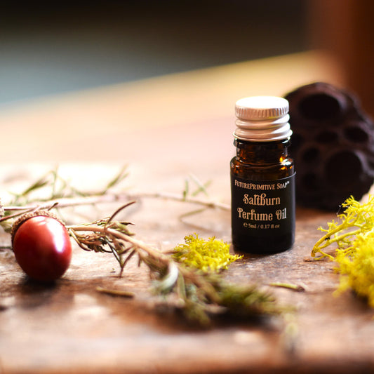 Perfume oil bottle labeled 'Saltburn' on a wooden surface with natural elements.