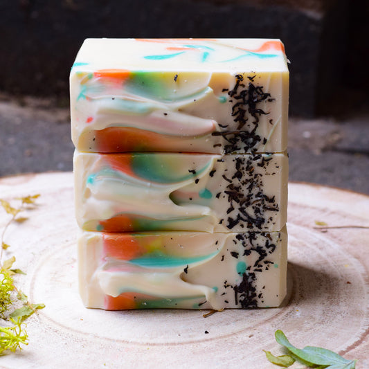Stack of colorful soap bars with black tea on a wooden surface