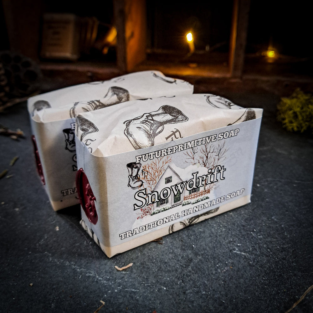 Two bars of 'Snowdrift' soap in a decorative box on a dark surface with a warm, blurred background.