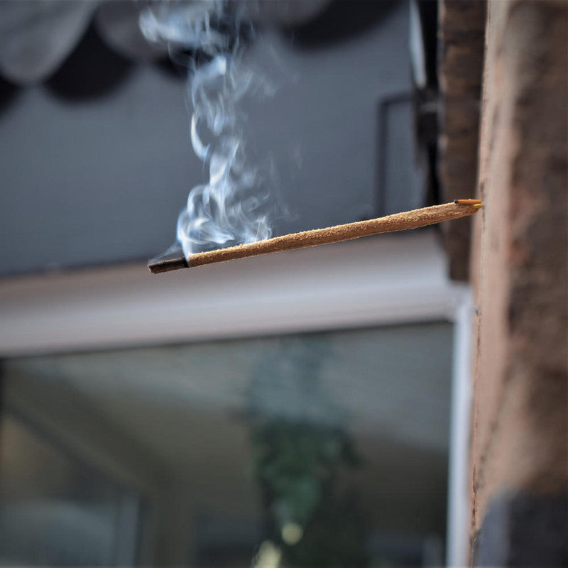 Sri Sai Flora Incense stick with smoke against a blurred indoor background