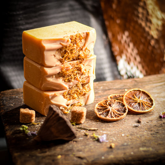 Stack of artisan handmade soap bars on a wooden surface with dried oranges and flowers.