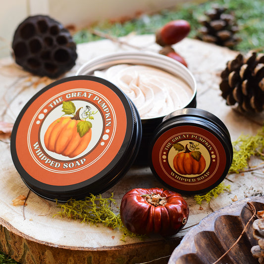 Two containers of 'The Great Pumpkin' whipped soap on a wooden surface with autumn-themed decorations.