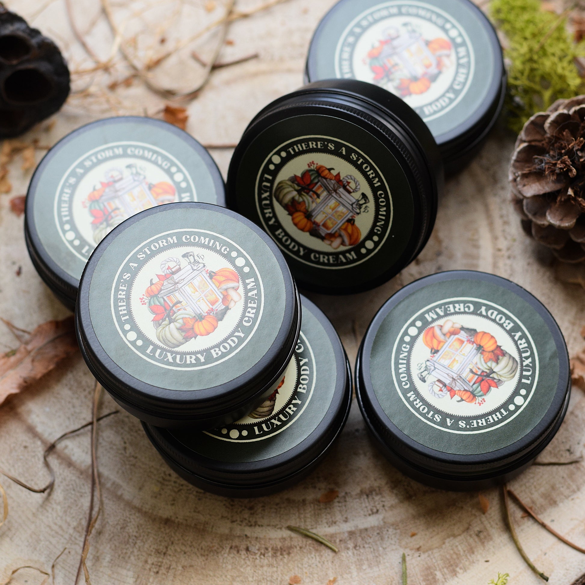Mini pots of There's a Storm Coming Luxury Body Cream in a natural setting with pine cones and moss