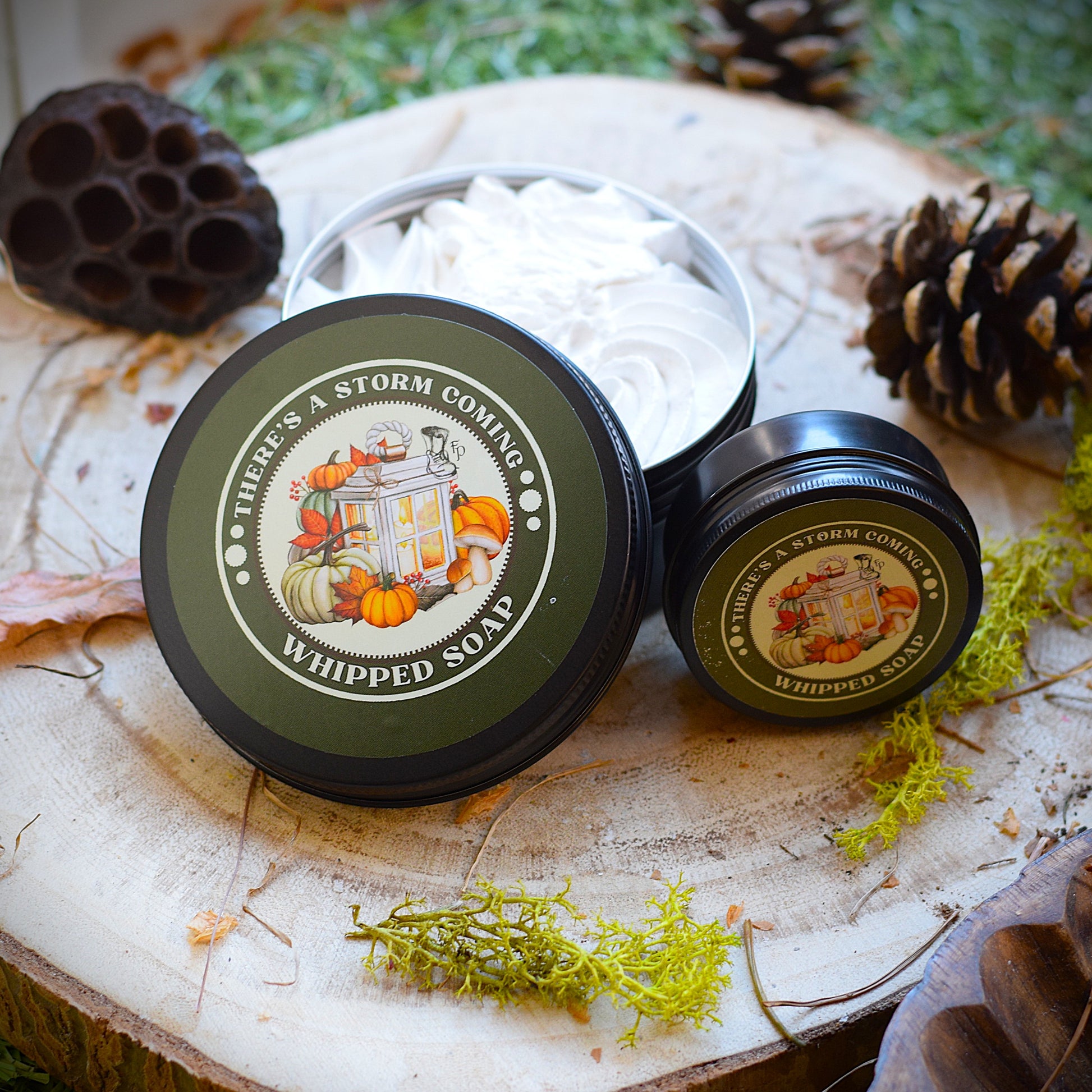 Two containers of 'There's a Storm Coming' whipped soap on a wooden surface with natural elements.