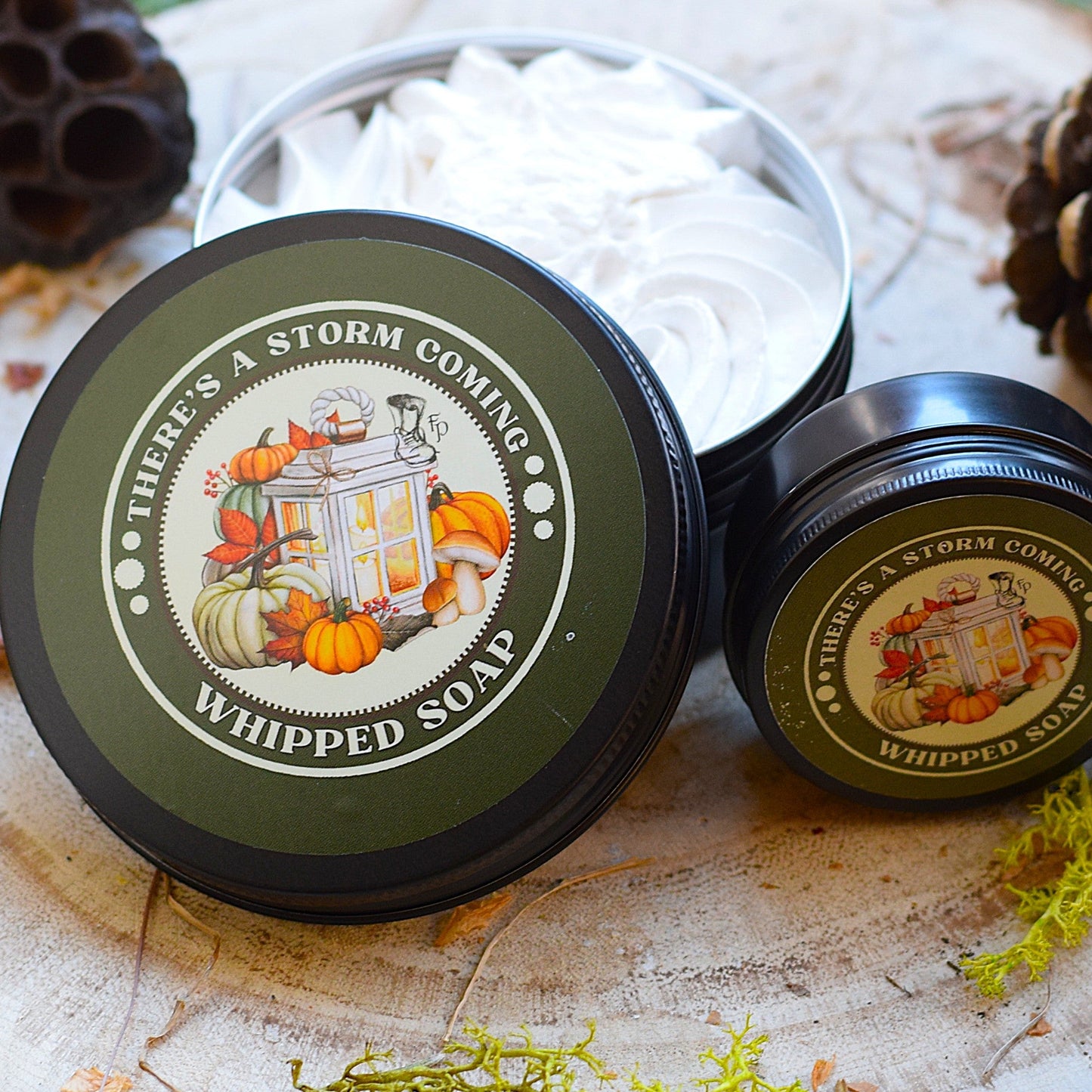 Two containers of 'There's a Storm Coming' whipped soap on a wooden surface with natural elements.