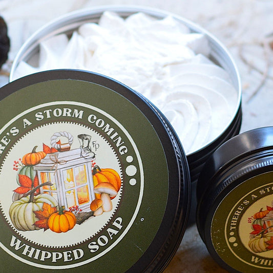 Two containers of 'There's a Storm Coming' whipped soap on a wooden surface with natural elements.