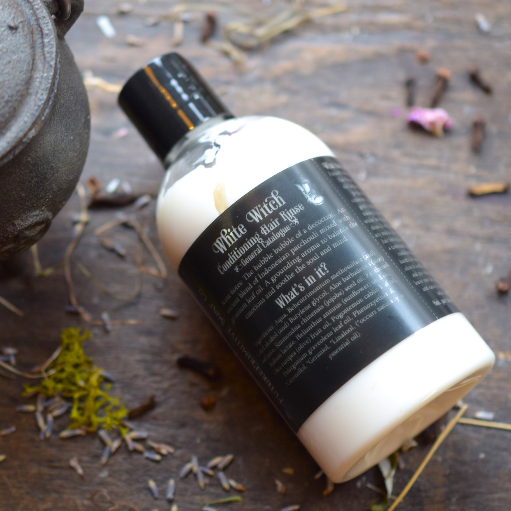 Bottle of Wilt's Witch Hair Tonic on a wooden surface with herbs and a teapot.