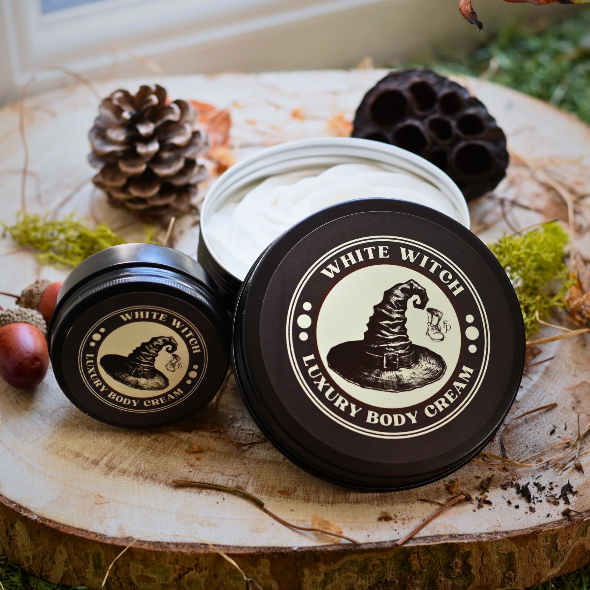 Two jars of 'White Witch Luxury Body Cream' on a wooden surface with natural elements.