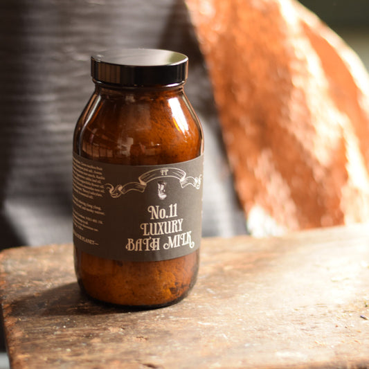 Brown jar labeled 'No.11 Luxury Bath Mud' on a wooden surface with a blurred background