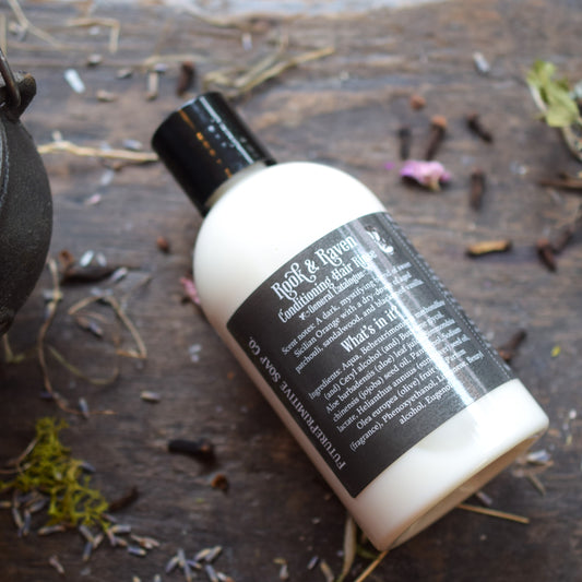 Bottle of 'Rook & Raven' hair product on a wooden surface with herbs.