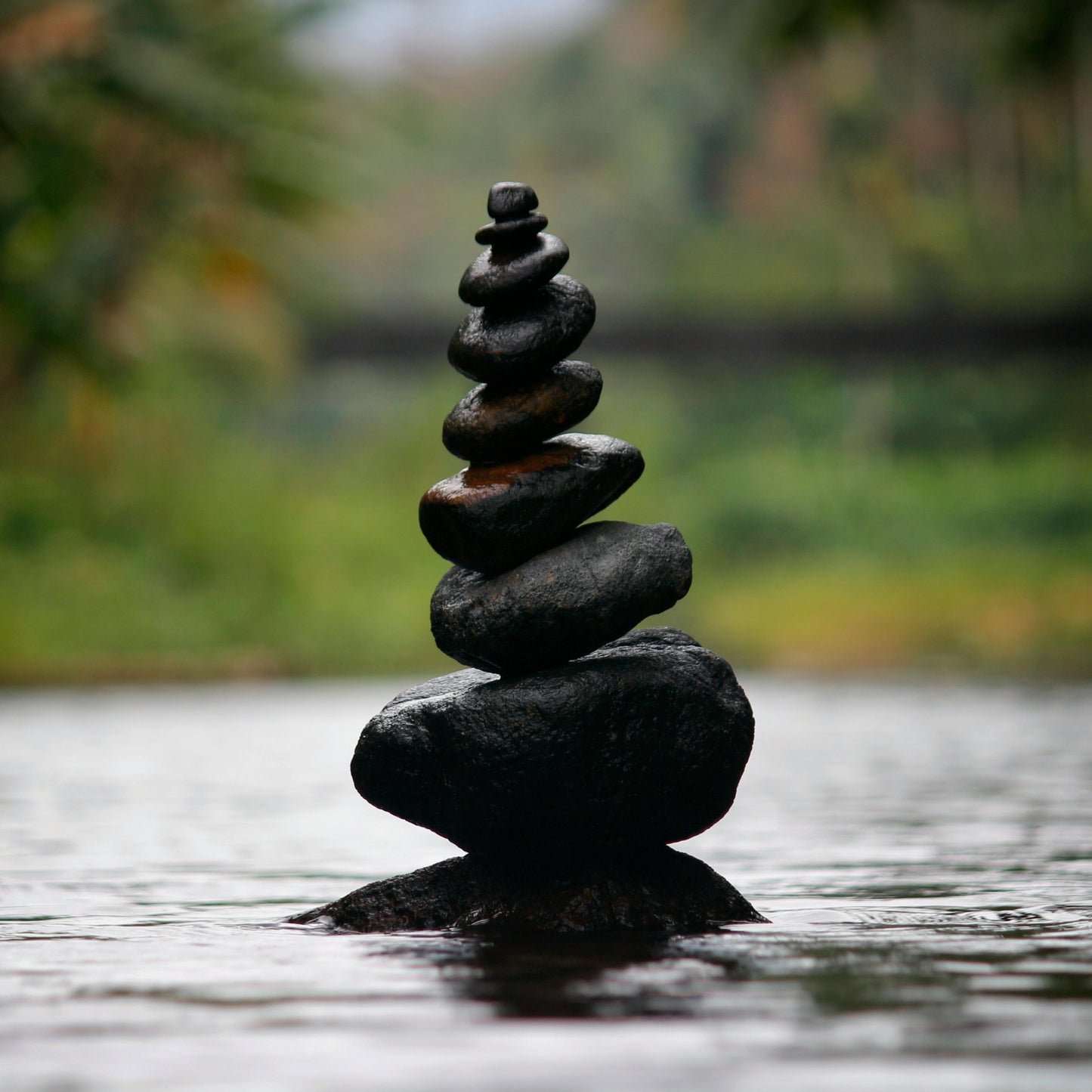 Stack of black stones balanced on water with a blurred natural background